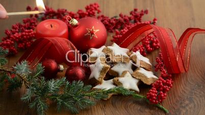 Kerze wird angezündet daneben Weihnachtsbaumkugeln und Tannengrün