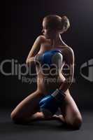Naked woman sit in dark with boxing gloves