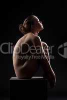 Beautiful nude woman sit in dark on cube