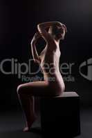 Beautiful nude woman sit in dark on cube