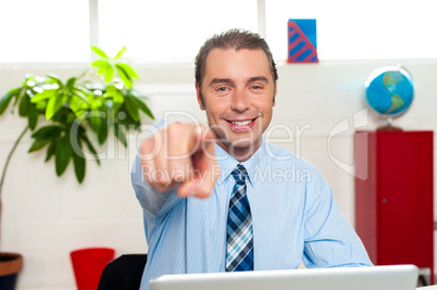 Businessman at work desk pointing at you