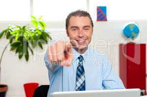 Businessman at work desk pointing at you