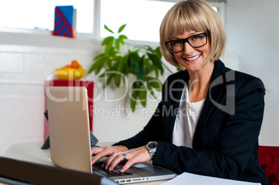 Smiling female manager typing report on laptop