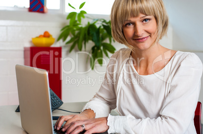 Blonde woman facing camera while working on laptop