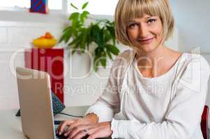 Blonde woman facing camera while working on laptop