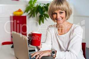 Cheerful woman holding coffee mug and working