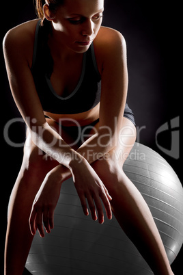 Thoughtful young woman relaxing on fitness ball