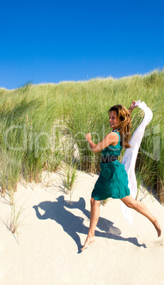 Frau springt mit Tuch durch die Dünen