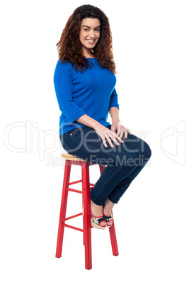 Long curly haired lady seated on red stool