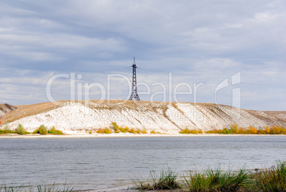 High voltage line and electricity pylon on coastline of river.