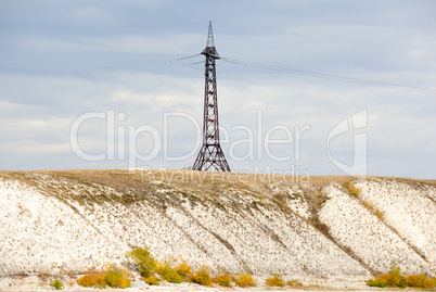 High voltage line and electricity pylon on coastline of river.