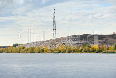 High voltage line and electricity pylon on coastline of river.