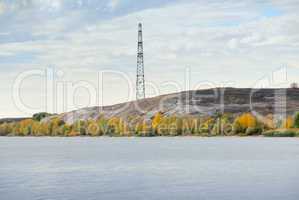 High voltage line and electricity pylon on coastline of river.