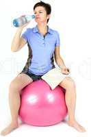 Woman sitting on exercise ball and drinks