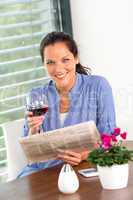 Cheerful woman reading drinking wine newspaper living