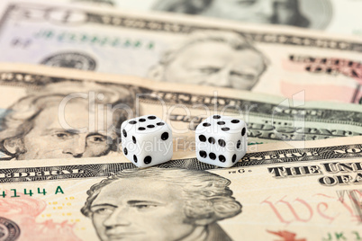 Two dice laying over a pile U.S. dollars