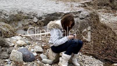 A girl sits on a stone with a telephone takes pictures
