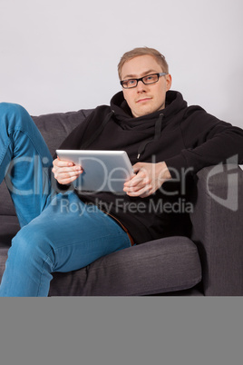 Ein junger Mann liegt auf einem Sofa und hat ein Tablet-PC in de