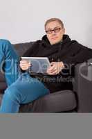 Ein junger Mann liegt auf einem Sofa und hat ein Tablet-PC in de