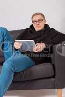 Ein junger Mann liegt auf einem Sofa und hat ein Tablet-PC in de