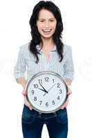 Cheerful brunette in casual presenting a wall clock