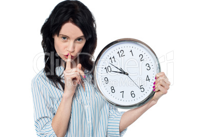 Young brunette with wall clock gesturing silence