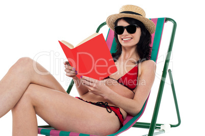 Enticing bikini model on a deckchair reading a book