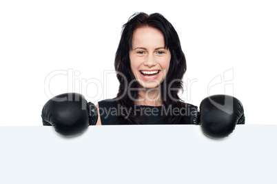 Woman with boxing gloves on posing behind billboard