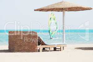 beach chair with straw sunshade at the sea and windsurfer