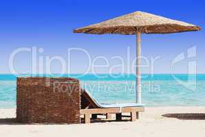 empty beach chair with straw sunshade at the sea