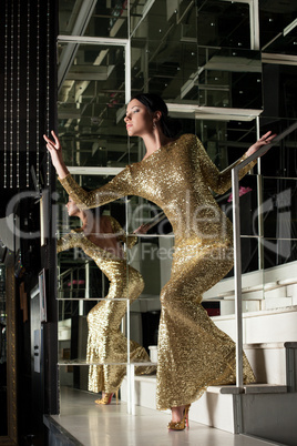 Pretty woman in beautiful gold dress on stairs