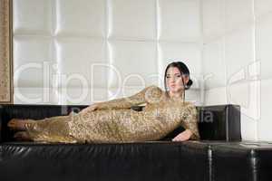 Fashion brunette woman in gold dress on sofa
