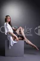 Sexy young brunette sitting on cube in studio