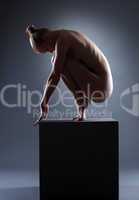 nude young woman posing on cube in dark