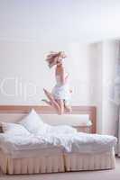 Happy young woman jumping on bed