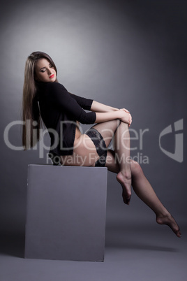 Beauty young brunette sitting on cube in studio