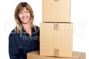 Cheerful delivery woman carrying sealed cartons