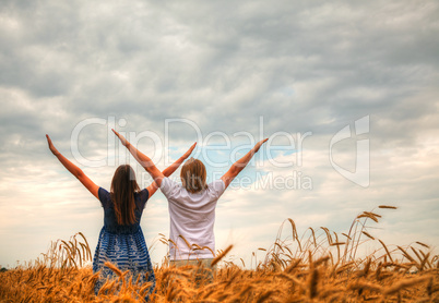 Couple staying with raised hands at a wheat field