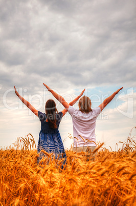 Couple staying with raised hands at a wheat field