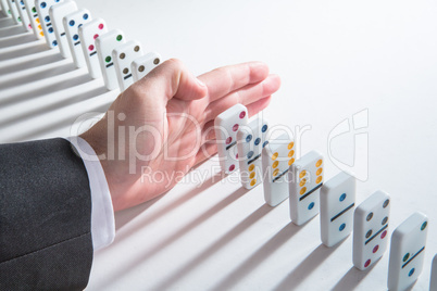 Hand resting in the middle of a line of dominoes about to push