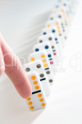 Finger about to knock over line of dominoes