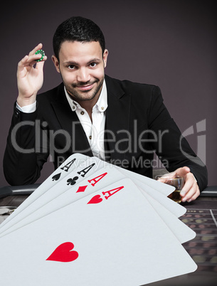 Handsome gambler betting on four aces at poker table