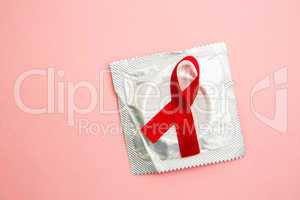 Red awareness ribbon lying on condom in wrapper