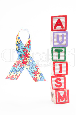 Autism awareness ribbon beside stacked blocks spelling autism