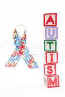 Autism awareness ribbon beside stacked blocks spelling autism