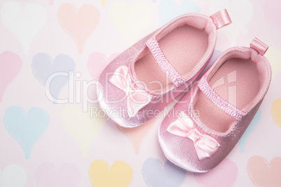 Baby pink booties on heart pattern background