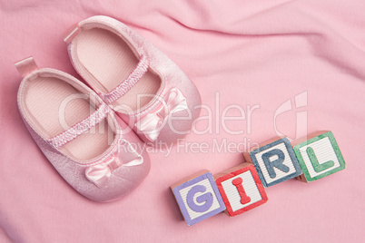 Pink baby slippers and blocks spelling girl