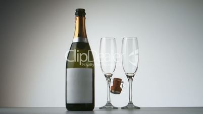 Champagne cork falling in front of bottle and flutes