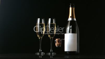 Champagne cork falling in front of flutes and bottle