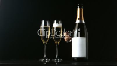 Champagne cork falling in front of  two flutes and bottle